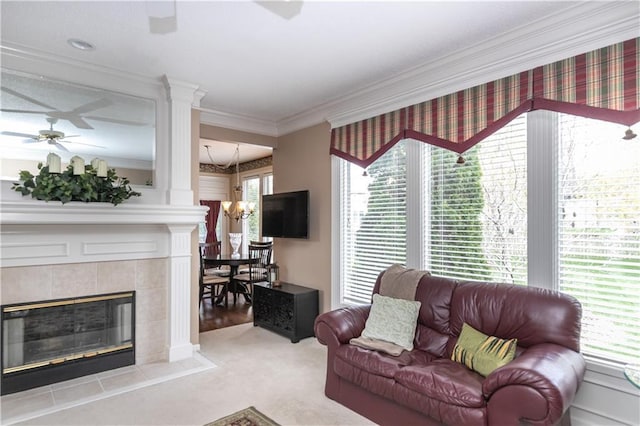 living room with a fireplace, crown molding, ornate columns, ceiling fan with notable chandelier, and light colored carpet