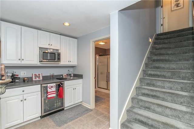 kitchen with wine cooler, stainless steel microwave, dark countertops, and white cabinetry
