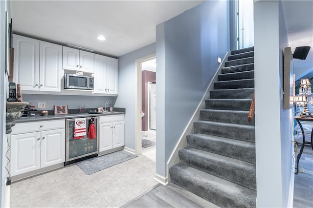 kitchen with wine cooler, stainless steel microwave, a sink, and white cabinets