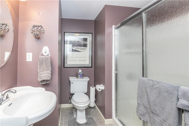 bathroom featuring toilet, a stall shower, a sink, and baseboards