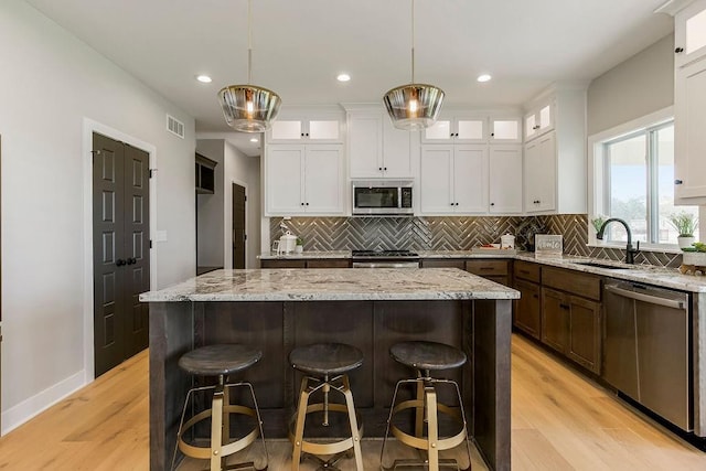 3141 SW Summit View Trl, Lees Summit, MO 64082 - kitchen featuring appliances with stainless steel finishes, a sink, white cabinets, light wood-style flooring, and tasteful backsplash