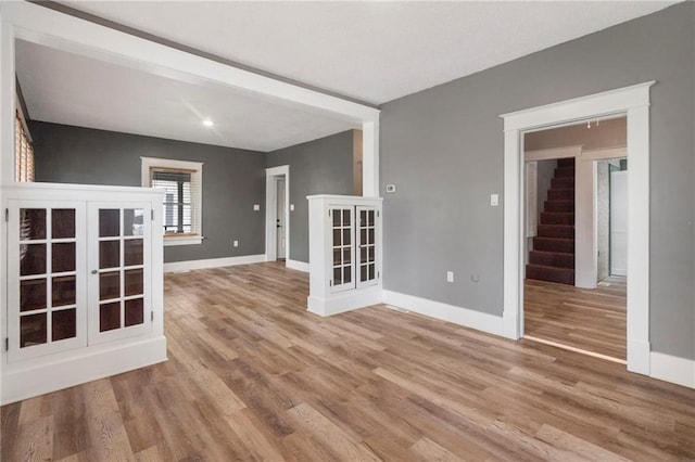 empty room with french doors, baseboards, wood finished floors, and stairway