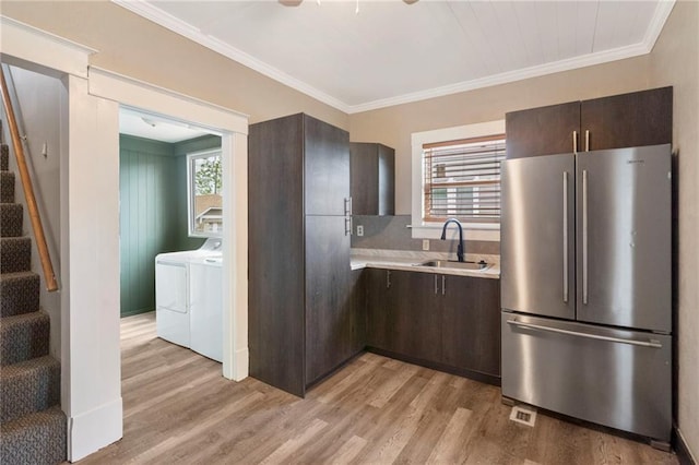 kitchen featuring freestanding refrigerator, dark brown cabinets, washer and clothes dryer, light countertops, and a sink