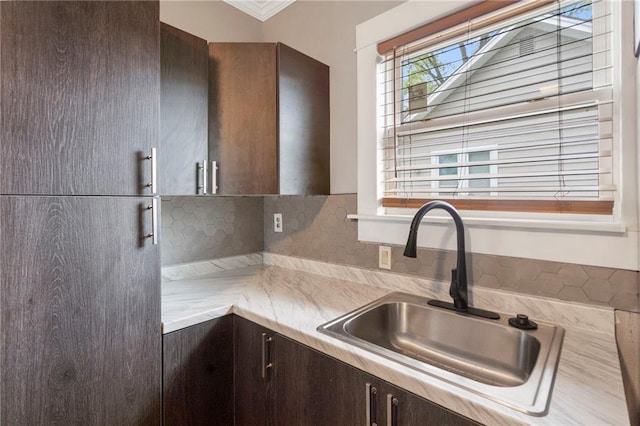 kitchen with backsplash, dark brown cabinets, a sink, and light countertops