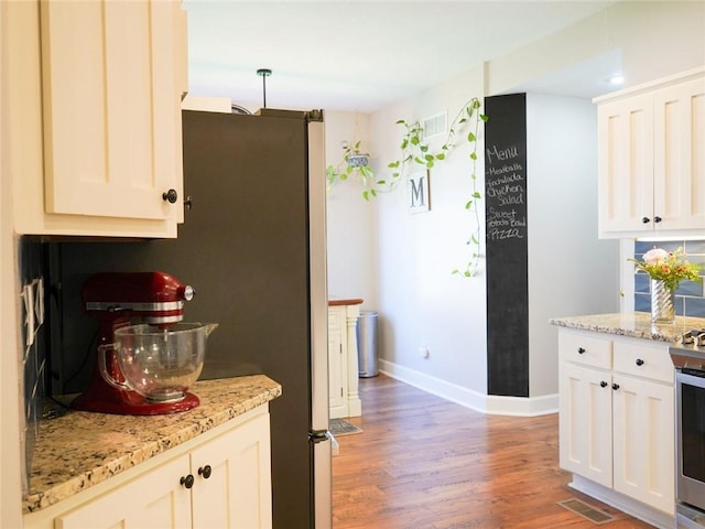 kitchen with light wood-type flooring, baseboards, visible vents, and light stone counters