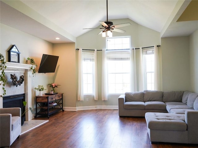 living room with dark wood finished floors, ceiling fan, a wealth of natural light, and a fireplace with raised hearth