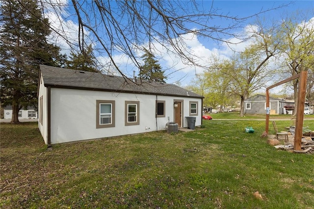 back of property featuring roof with shingles, stucco siding, and a lawn
