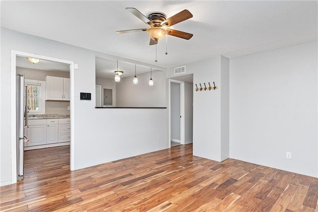empty room featuring visible vents, a ceiling fan, light wood-style floors, and electric panel