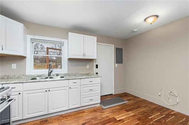 kitchen with baseboards, stainless steel range with gas cooktop, white cabinets, light wood-style floors, and a sink