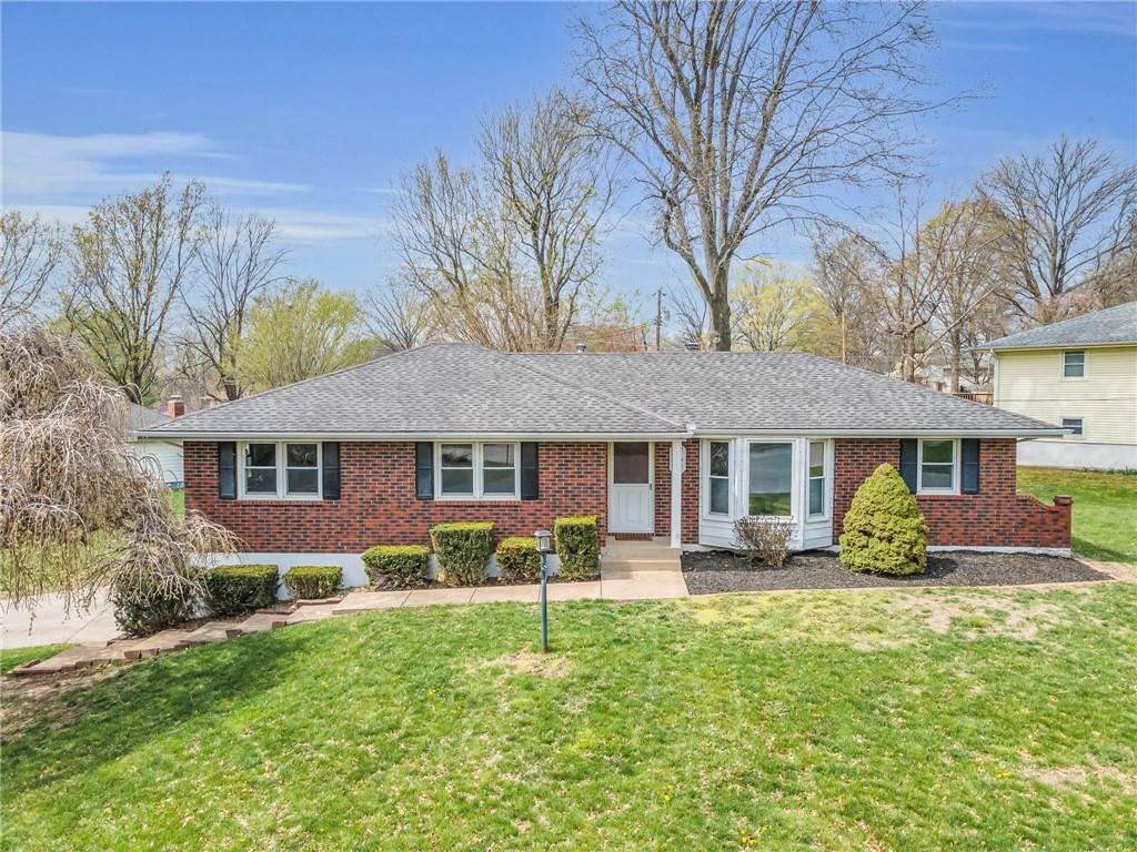 ranch-style house featuring roof with shingles, brick siding, and a front lawn