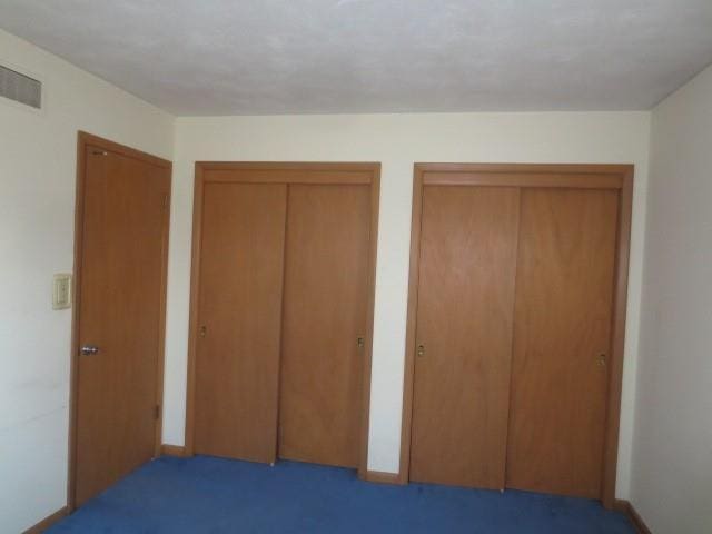 unfurnished bedroom featuring visible vents, multiple closets, baseboards, and carpet floors