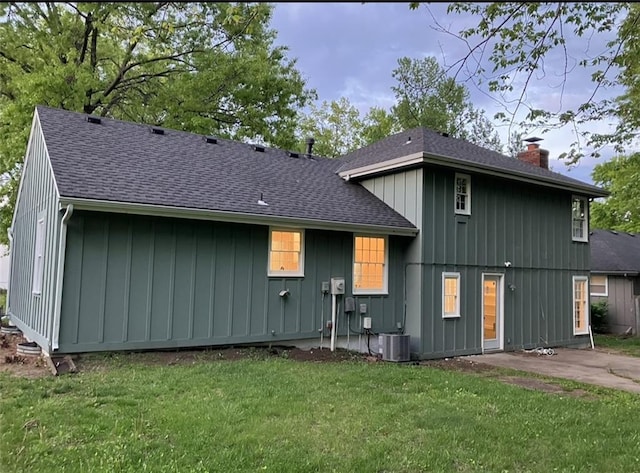 back of house with a yard, central AC, board and batten siding, and a chimney