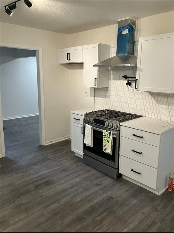 kitchen with dark wood-style flooring, stainless steel range with gas stovetop, wall chimney exhaust hood, white cabinetry, and backsplash