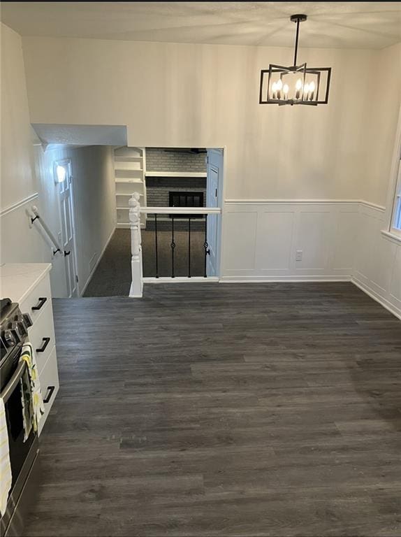 unfurnished dining area with an inviting chandelier, dark wood-style floors, and a wainscoted wall