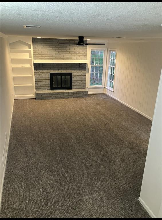 unfurnished living room with a textured ceiling, visible vents, carpet, and a fireplace