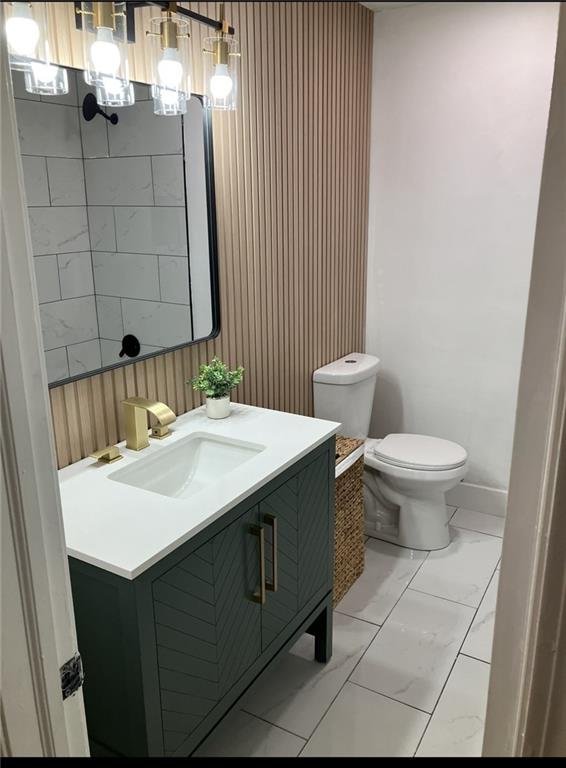 bathroom featuring wooden walls, vanity, toilet, and marble finish floor