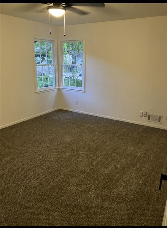 unfurnished room with baseboards, a ceiling fan, dark carpet, and visible vents