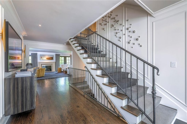 stairway featuring a glass covered fireplace, ornamental molding, and wood finished floors