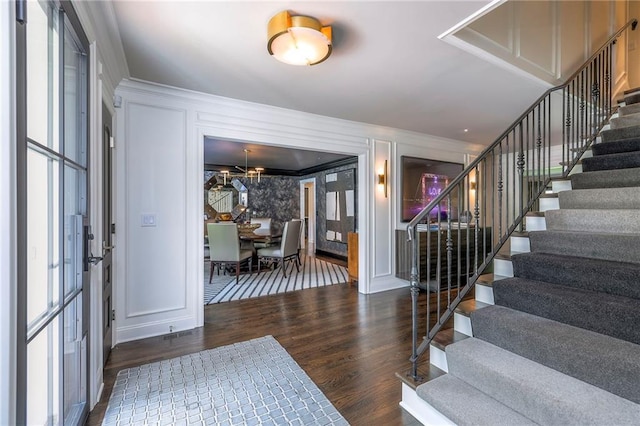 entryway featuring ornamental molding, a decorative wall, stairs, and wood finished floors