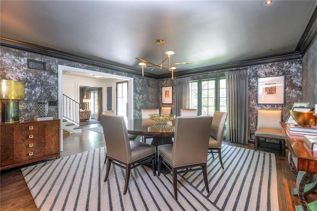 dining area with a chandelier, wallpapered walls, wood finished floors, ornamental molding, and stairway
