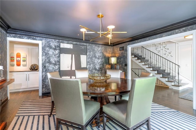 dining space featuring crown molding, wallpapered walls, a notable chandelier, and wood finished floors