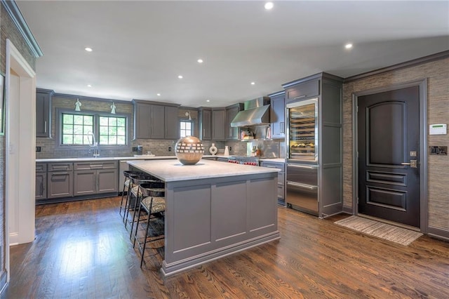 kitchen with a kitchen island, wall chimney range hood, light countertops, tasteful backsplash, and gray cabinetry
