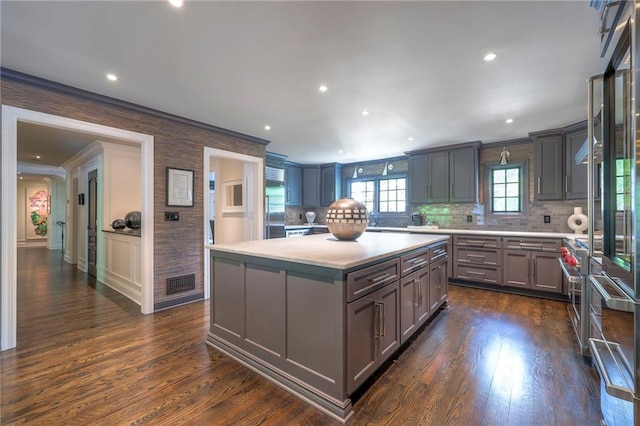 kitchen featuring decorative backsplash, crown molding, a center island, gray cabinetry, and light countertops