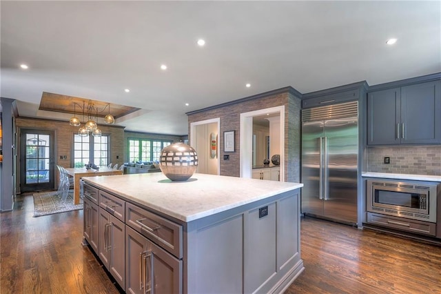 kitchen with dark wood-style flooring, a center island, tasteful backsplash, a raised ceiling, and built in appliances