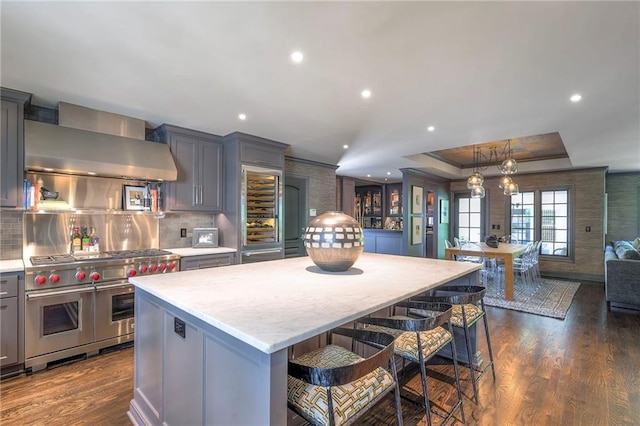 kitchen featuring gray cabinets, a kitchen island, range with two ovens, dark wood finished floors, and wall chimney exhaust hood