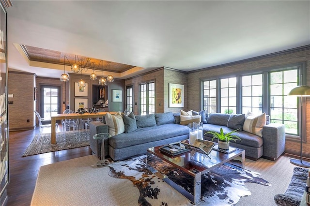 living area featuring ornamental molding, a tray ceiling, wood finished floors, and a chandelier