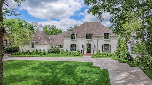 french country style house with stucco siding, a chimney, and a front lawn
