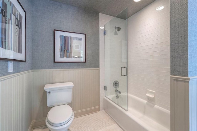 bathroom with a wainscoted wall, bathing tub / shower combination, and toilet