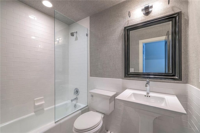 full bath featuring combined bath / shower with glass door, tile walls, wainscoting, and toilet