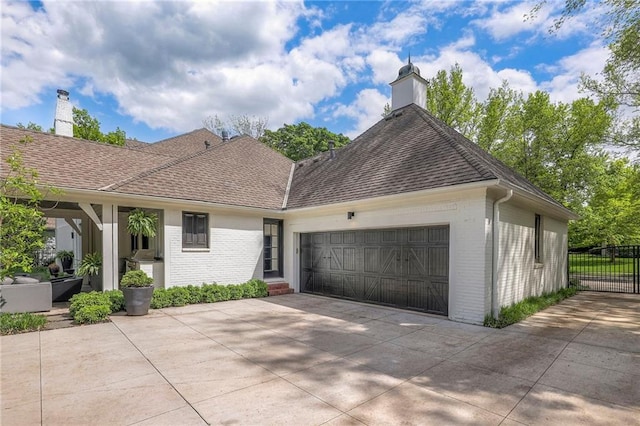 single story home featuring a chimney, roof with shingles, a garage, brick siding, and concrete driveway