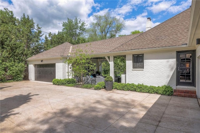 exterior space featuring a chimney, brick siding, concrete driveway, an attached garage, and a shingled roof