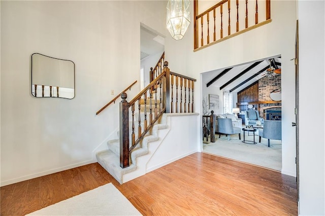 stairs featuring baseboards, a high ceiling, wood finished floors, and a fireplace