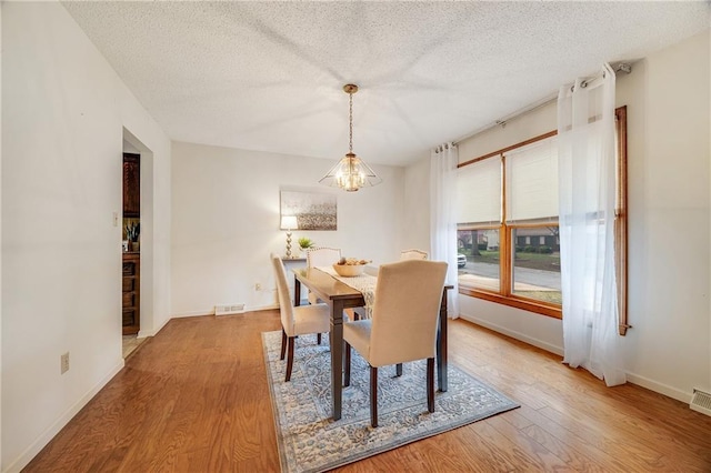 dining space with visible vents, baseboards, a notable chandelier, a textured ceiling, and wood finished floors