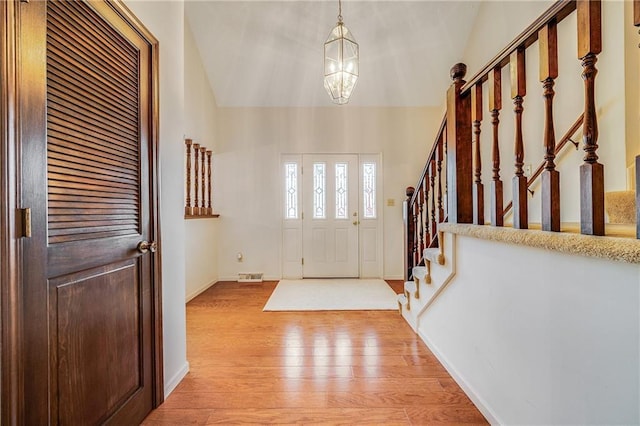 entrance foyer with visible vents, baseboards, a chandelier, light wood-style floors, and stairs