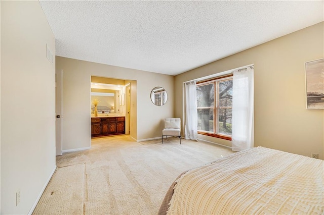 bedroom with ensuite bathroom, light colored carpet, baseboards, and a textured ceiling