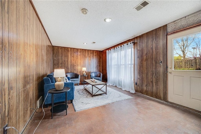 living area with wooden walls, visible vents, a textured ceiling, and a healthy amount of sunlight