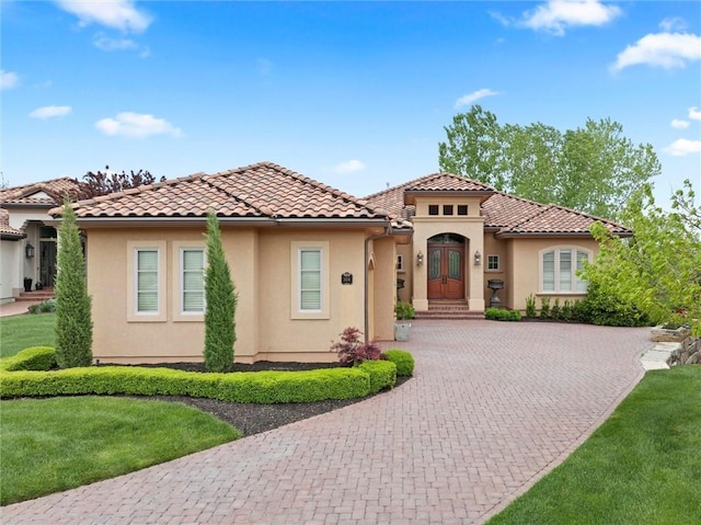 mediterranean / spanish-style house with a front yard, curved driveway, stucco siding, french doors, and a tile roof