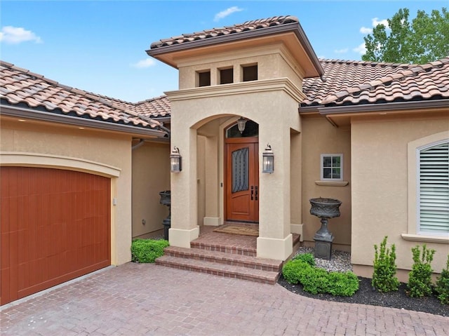 view of exterior entry with decorative driveway, an attached garage, a tile roof, and stucco siding