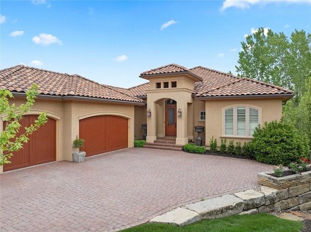 mediterranean / spanish home with a tiled roof, decorative driveway, a garage, and stucco siding