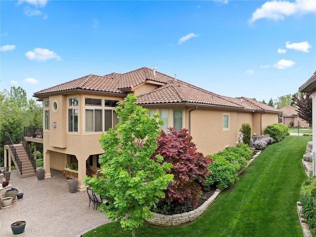 view of property exterior featuring stairs, a tile roof, stucco siding, a lawn, and a patio