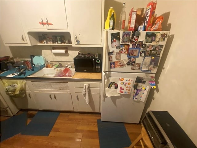 8733 E Saint John Ave, Kansas City, MO 64053 - kitchen featuring a sink, freestanding refrigerator, black microwave, white cabinetry, and wood finished floors