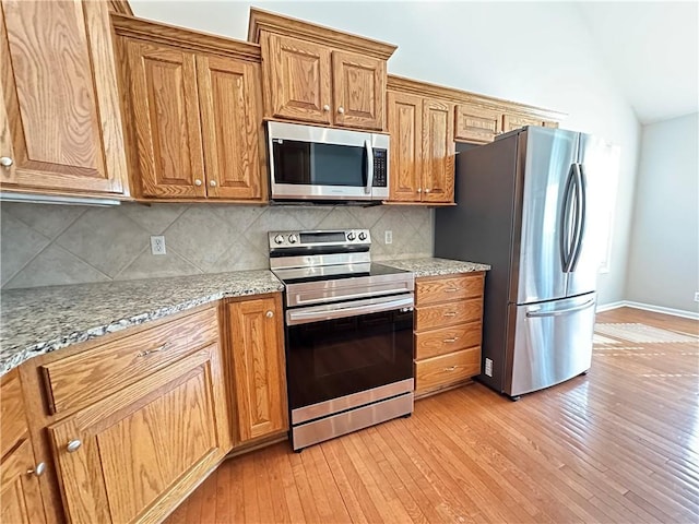 109 Deerfield Dr, Warrensburg, MO 64093 - kitchen featuring appliances with stainless steel finishes, brown cabinets, vaulted ceiling, light wood-style flooring, and decorative backsplash