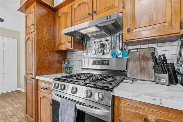 kitchen with stainless steel range with gas stovetop, under cabinet range hood, light countertops, decorative backsplash, and brown cabinetry