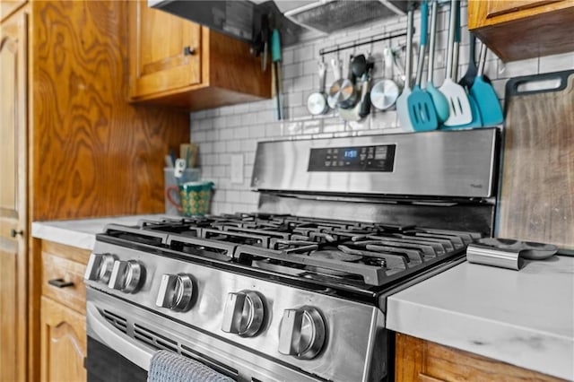 kitchen view of stainless steel gas stove, decorative backsplash, brown cabinets, and light countertops