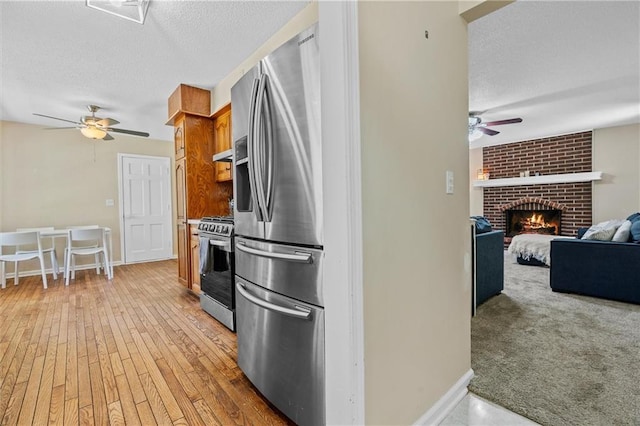 kitchen featuring appliances with stainless steel finishes, ceiling fan, a textured ceiling, a brick fireplace, and baseboards