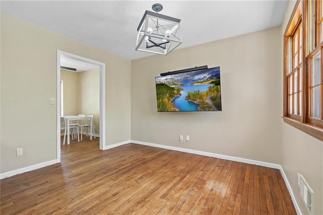 spare room with a chandelier, hardwood / wood-style floors, and baseboards